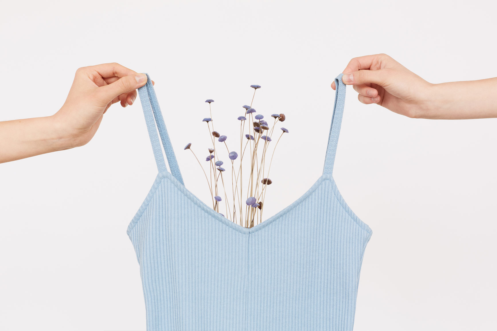 Two female hands holding light blue bodysuit decorated with small purple flowers close up shot