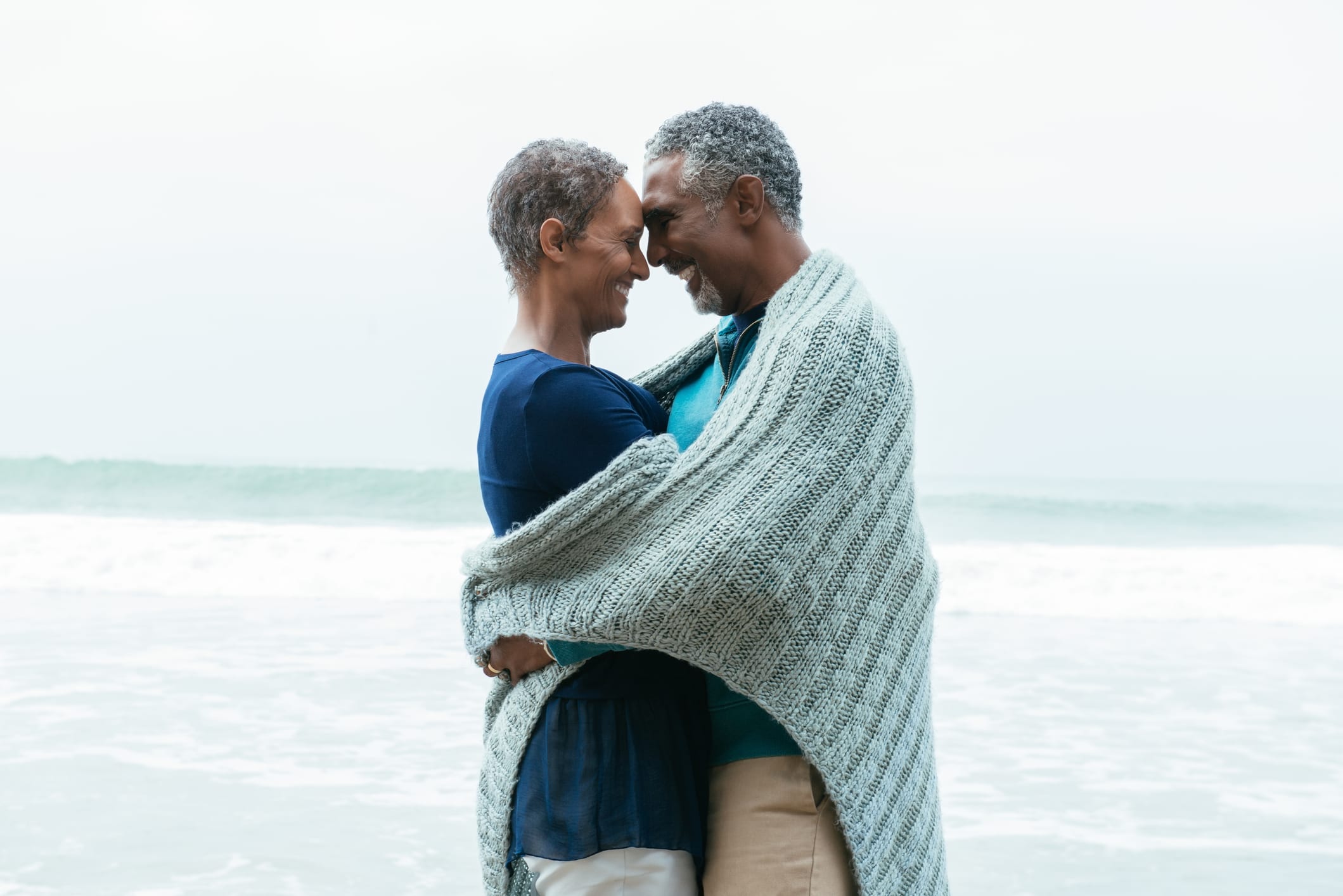 Happy mature woman embracing male partner at beach against sea