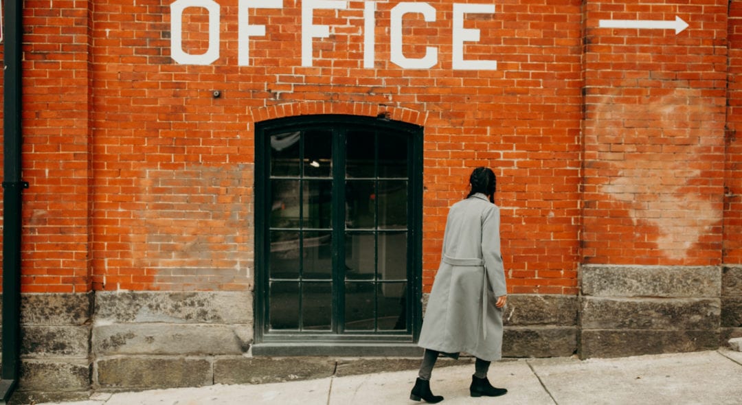 girl walking by a brick building with a window looking at an office sign
