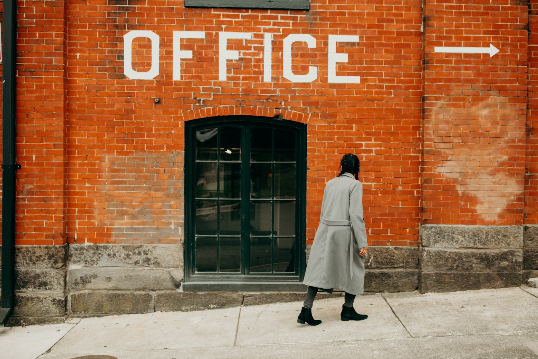 girl walking by a brick building with a window looking at an office sign
