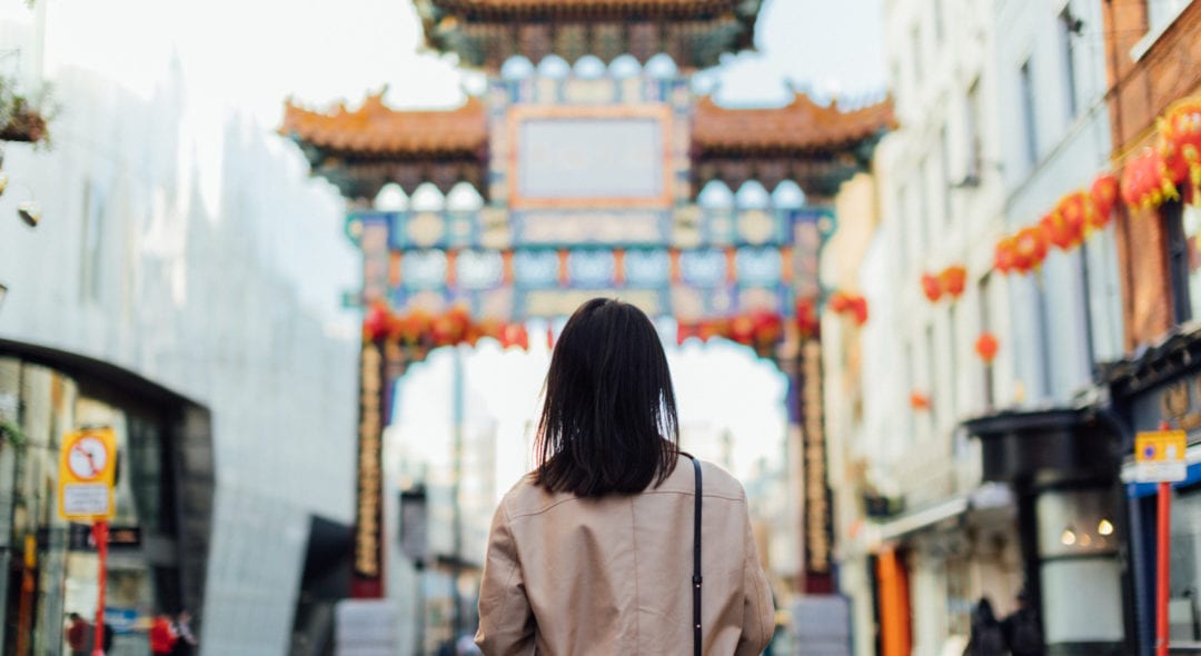 Rear view of a female tourist walking on the street at Chinatown, facing a traditional Chinese style pavilion in Chinatown, London - with red coloured lantern hanging in the sky.