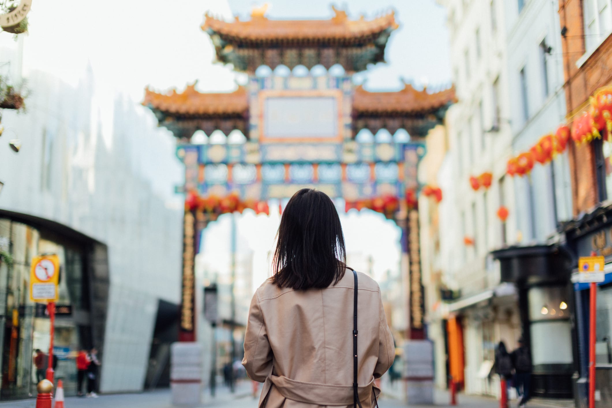 Rear view of a female tourist walking on the street at Chinatown, facing a traditional Chinese style pavilion in Chinatown, London - with red coloured lantern hanging in the sky.