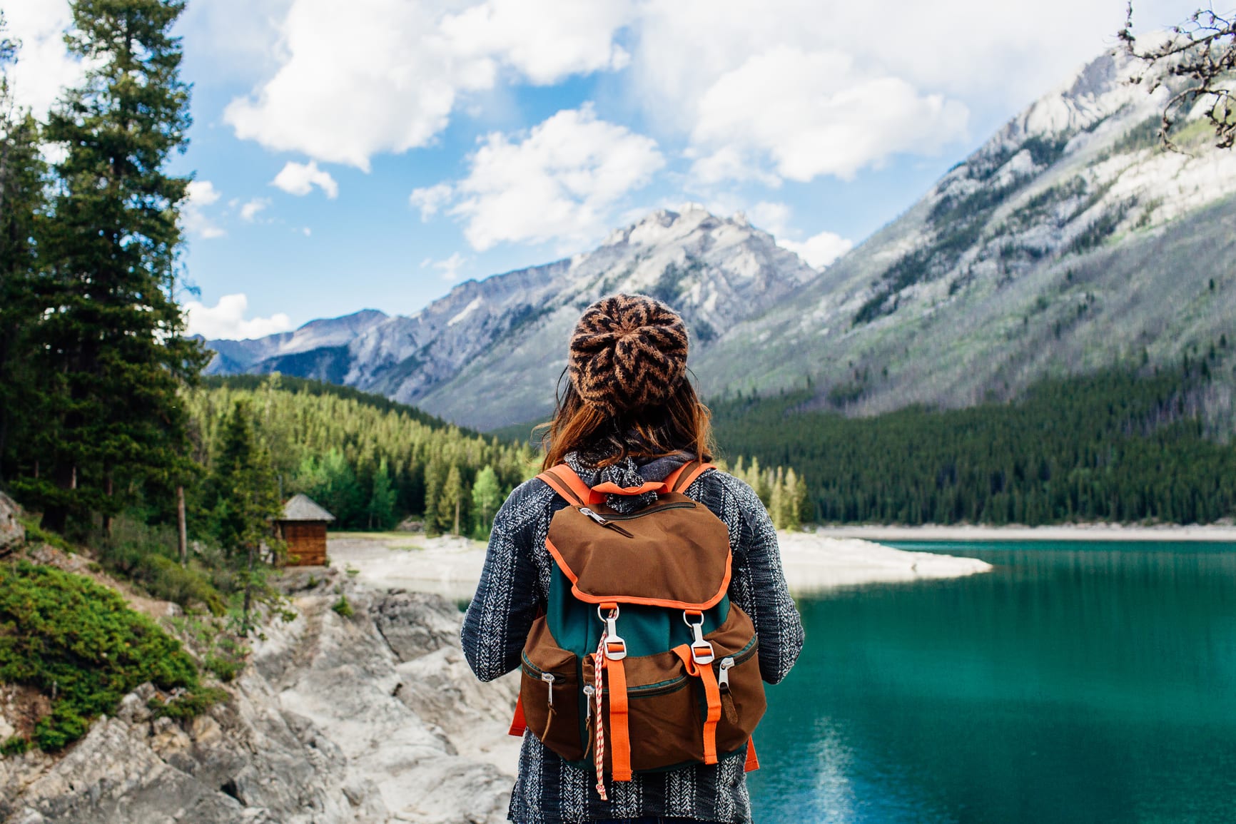 A Woman Wearing A Backpack Looking Out Towards A Blue Lake