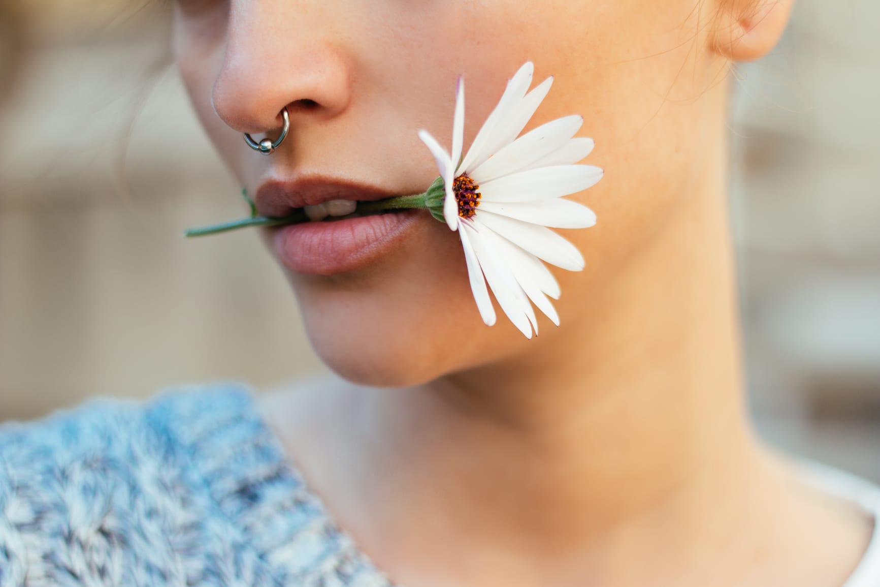 Woman with pierced septum and a daisy in her mouth