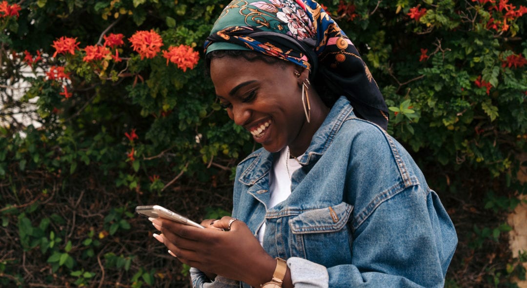 Black woman laughing and texting on her cell phone.