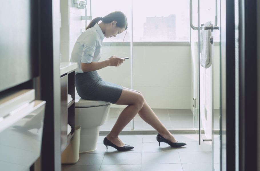 woman sitting on flush toilet typing smartphone.