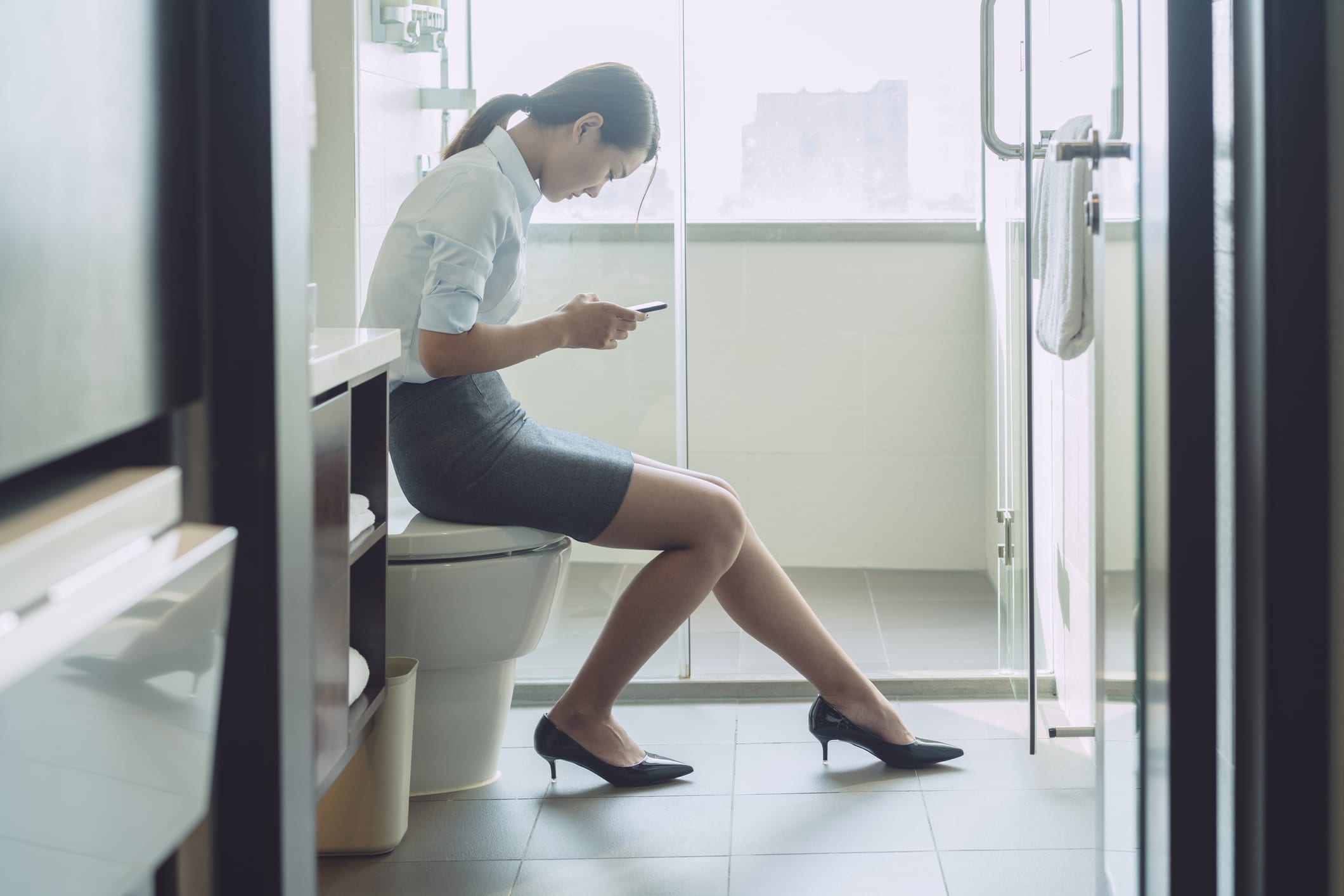 woman sitting on flush toilet typing smartphone.