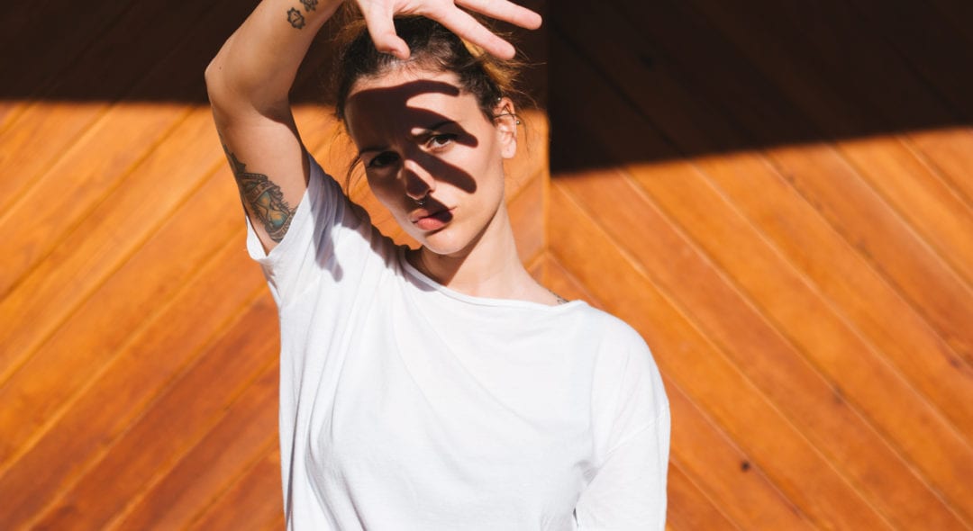 Portrait of young woman wearing white shirt, which cover the sun with your hand