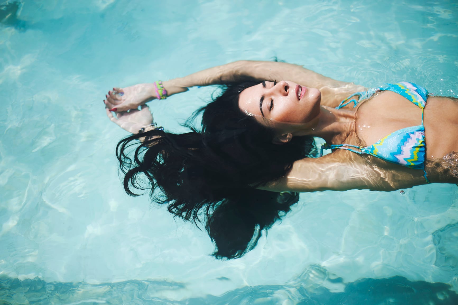 An attrative young woman with black hair floating on the water.