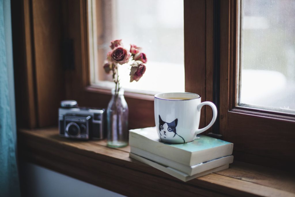 Cute mug with books, flowers and old camera on a window sill