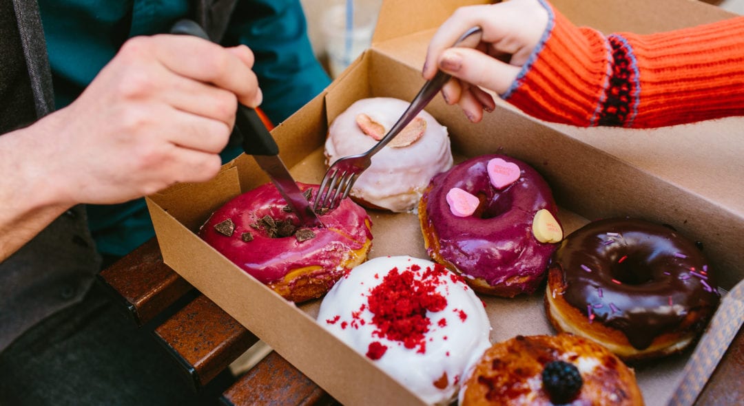Horizontal photo of a man & woman sharing a box of delicious looking donuts
