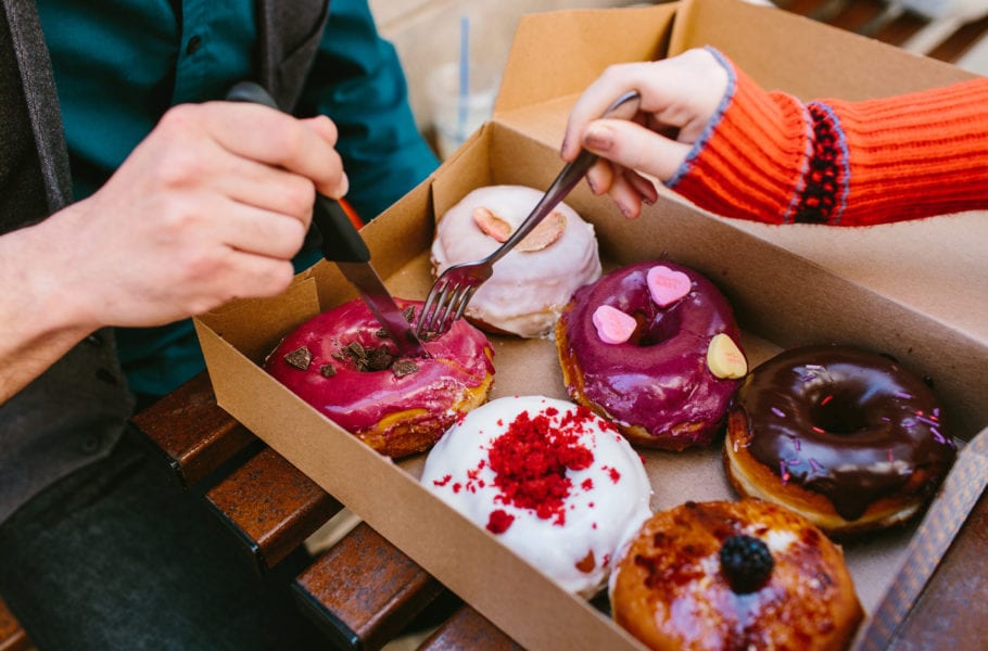 Horizontal photo of a man & woman sharing a box of delicious looking donuts