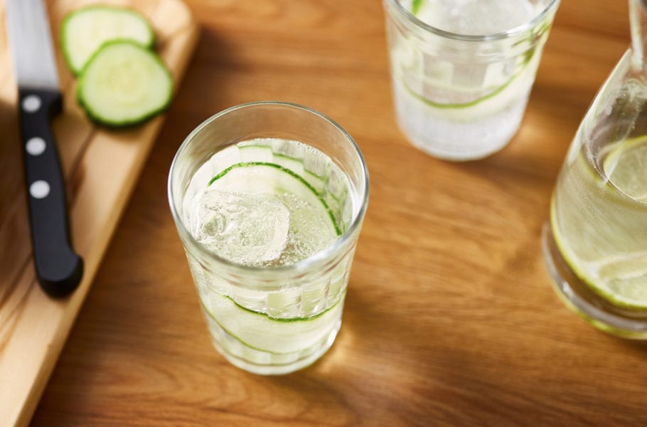 Glasses of fresh cold sparkling water with cucumber on table
