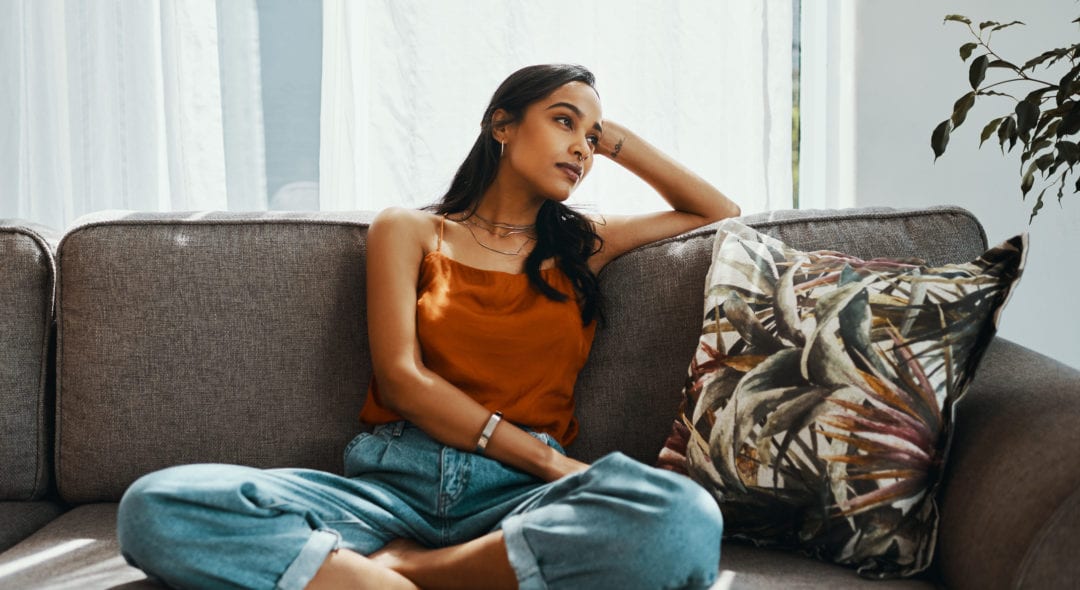 Shot of a young woman looking thoughtful while relaxing on the sofa at home