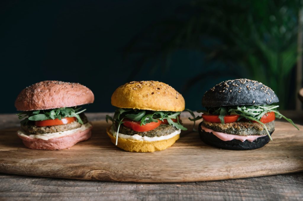 Colorful vegan hamburgers on wooden cutting board with vegan patty and toppings