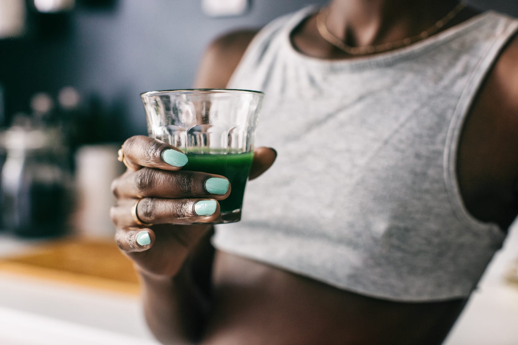 Closeup of an anonymous black woman with a glass of fresh green juice.