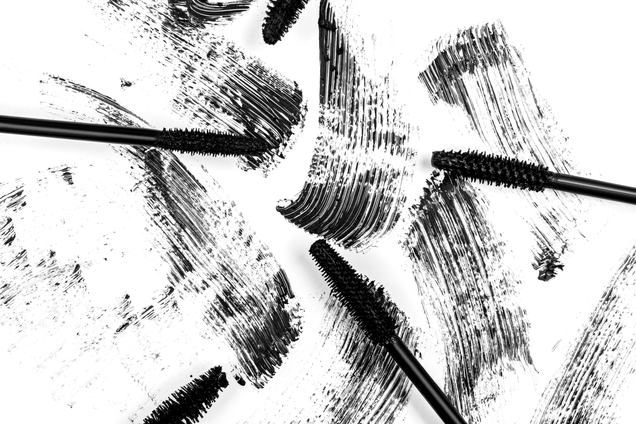 Black smear mascara and brushes on white background. Isolated. Makeup. Cosmetic products for eyelashes. Closeup. Beautiful pattern.