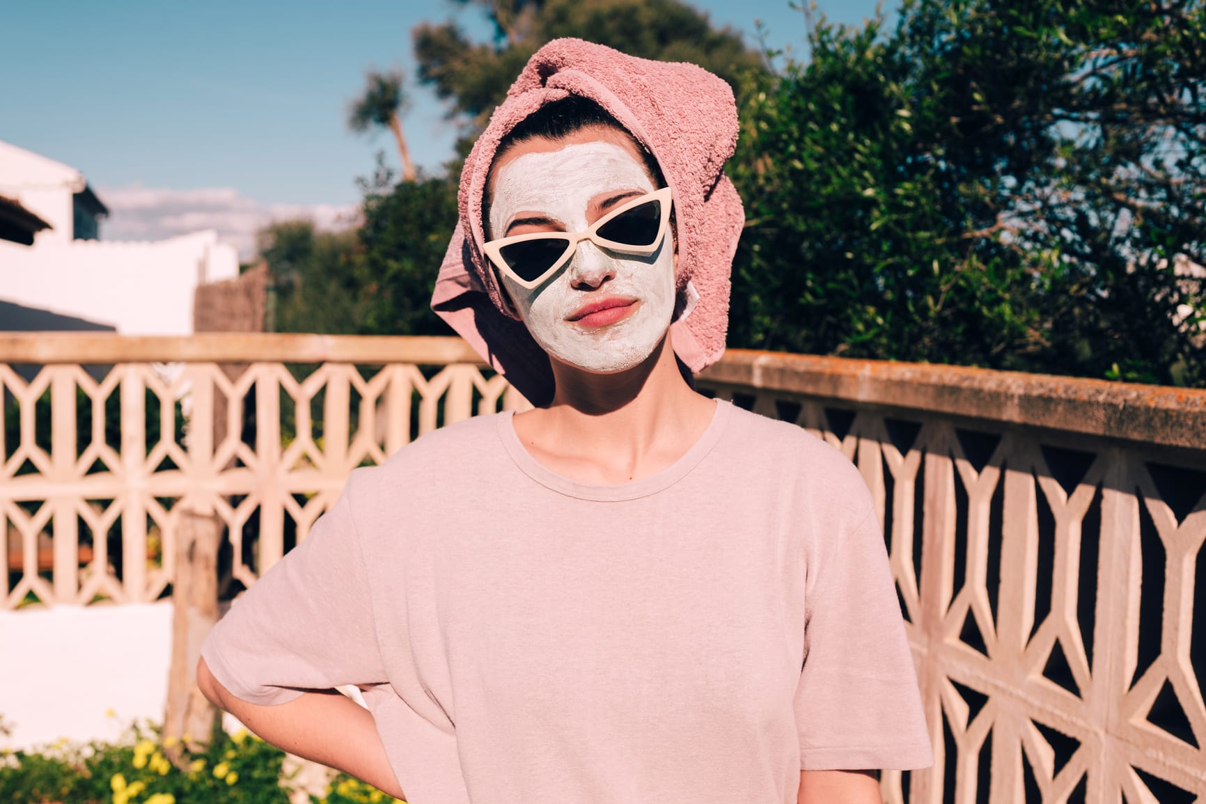 Young woman with white face mask and sunglasses, wearing a towel on her hair, looking at camera.