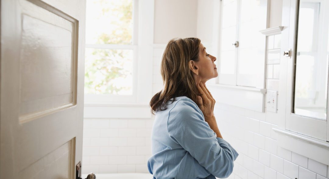 Woman looking in bathroom mirror, touching neck