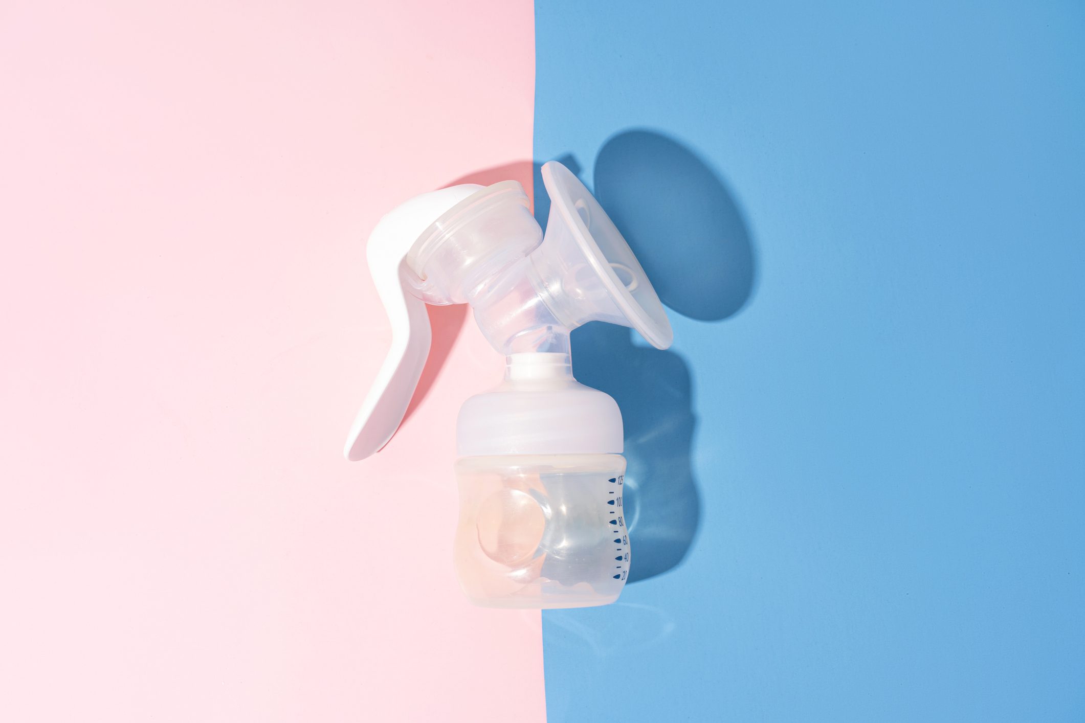 Manual breast pump on blue and pink background with hard shadows.