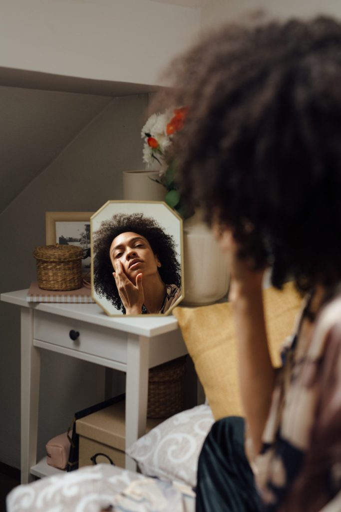 The woman applies the lotion to her face and looks in the mirror in her bedroom. The focus is on the mirror.