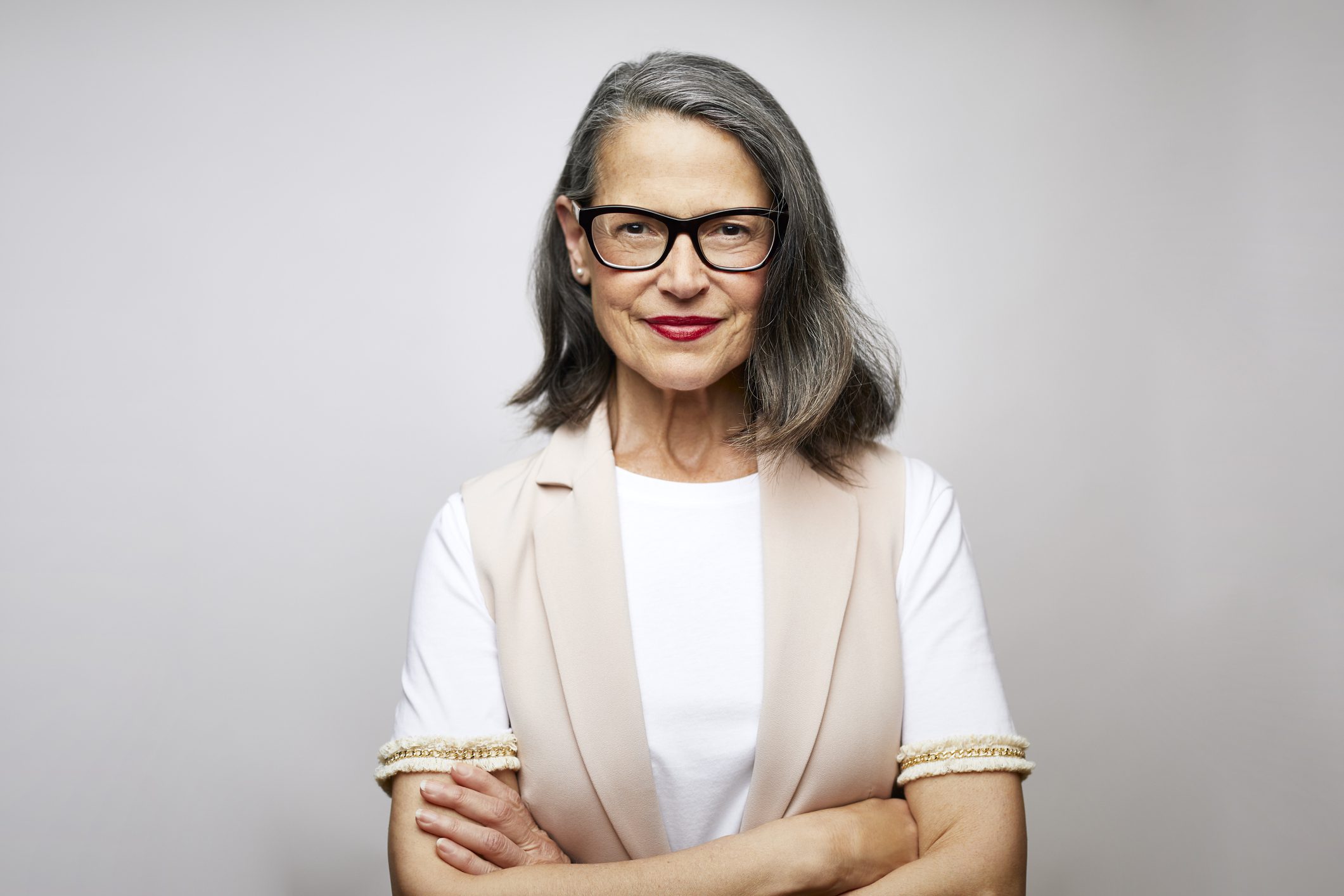Mature female CEO with arms crossed. Confident businesswoman is against white background. Portrait of smiling design professional.