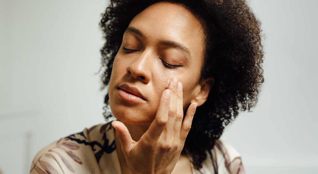 Close up of a young anonymous brunette woman with her eyes closed moisturizing her skin.
