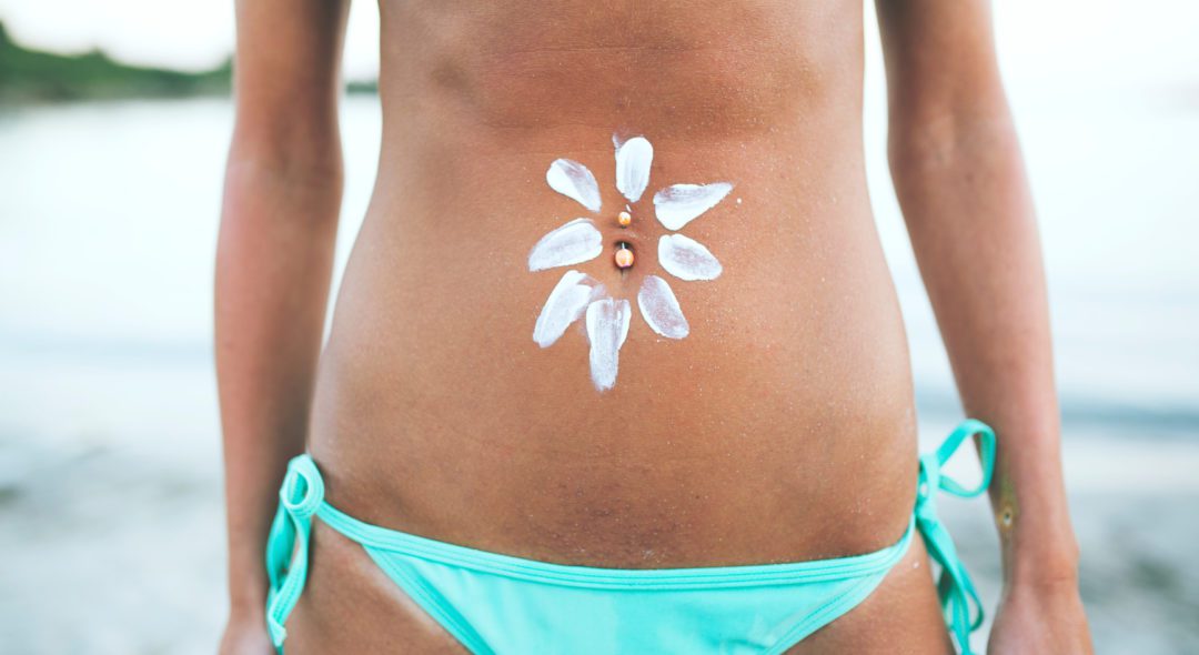 Sunscreen lotion over tan woman belly skin made as sun shape