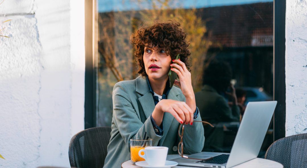 A beautiful woman sitting in a cafe, talking on the phone, working on her laptop