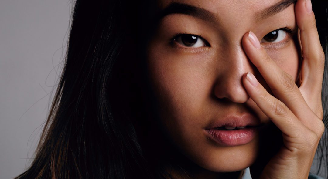 Close-up of calm Korean girl with smooth skin looking at camera with fingers on face