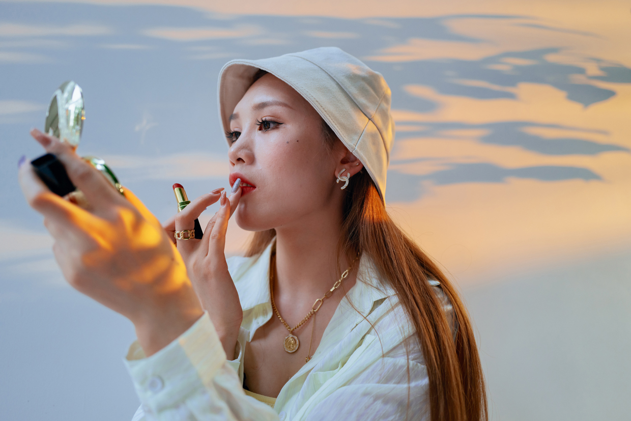 Young asian woman applying red lipstick outside