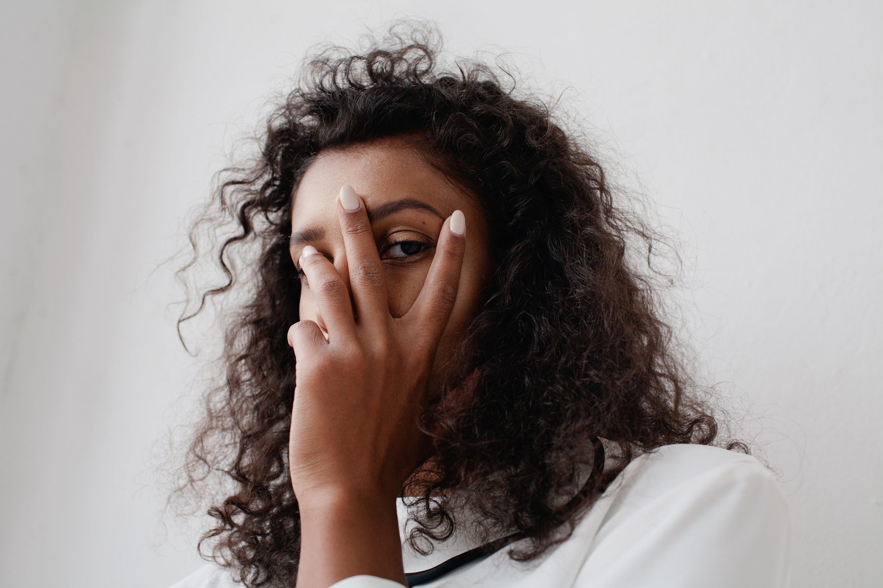Young african american woman with beautiful curly hair hide her face and posing on white background