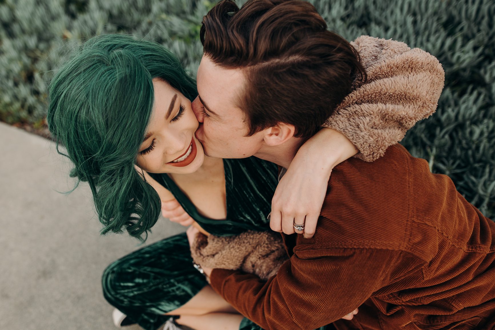 Trendy vintage couple with arms wrapped around each other with boyfriend kissing girlfriend's cheek
