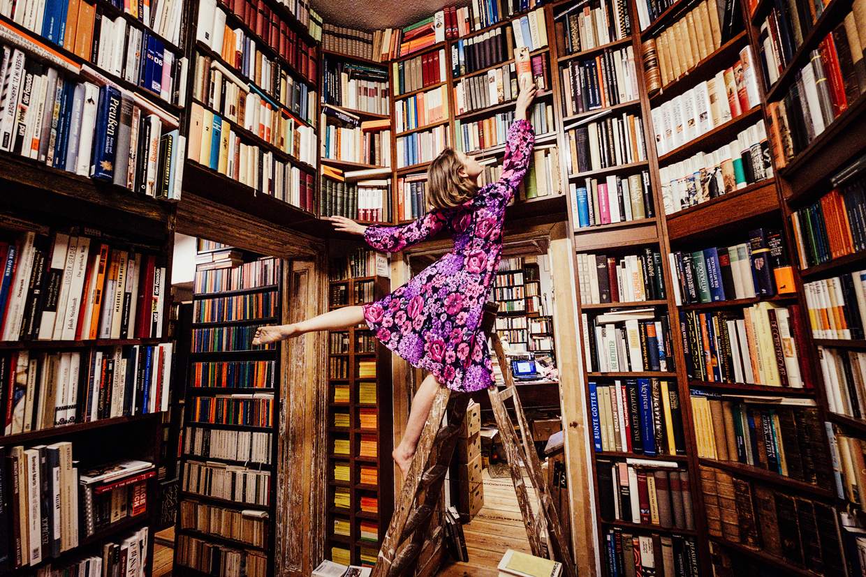 woman on ladder reaching for book in library