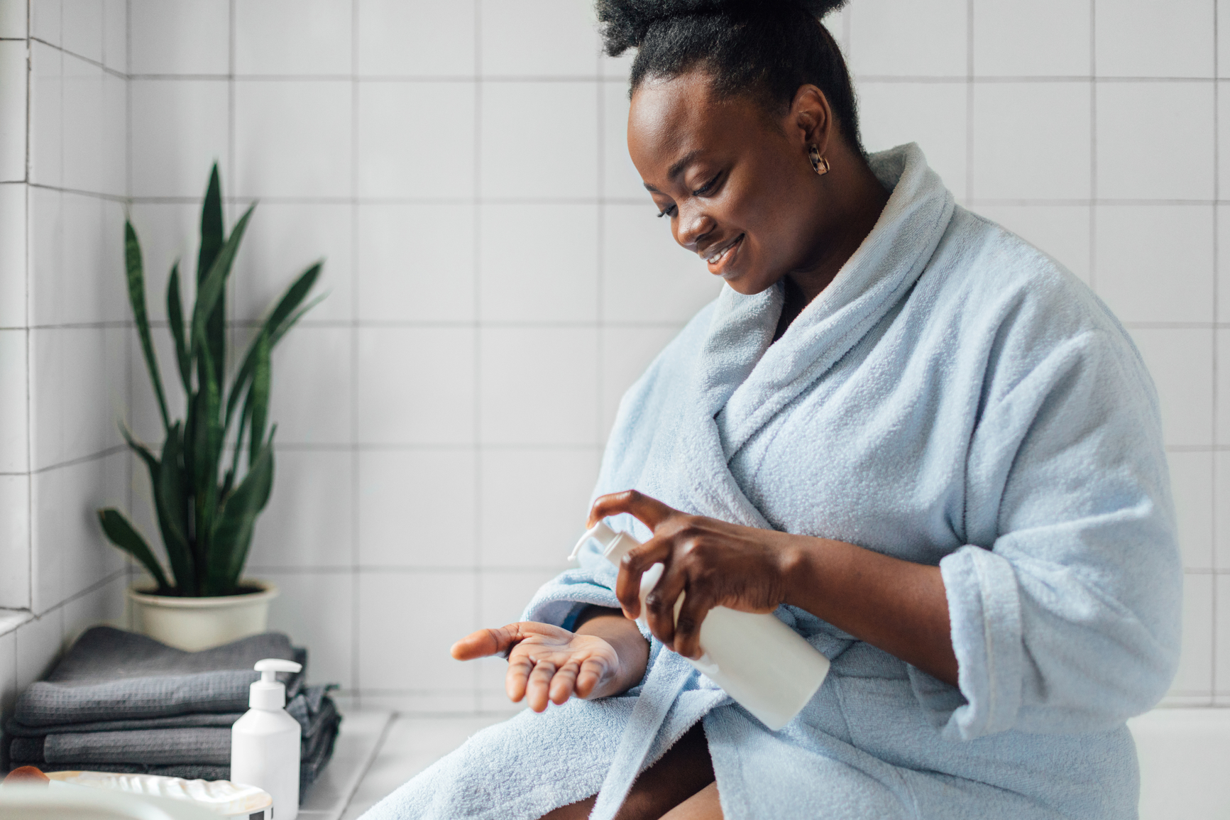 african american woman sitting on the tub in the bathroom using body lotion