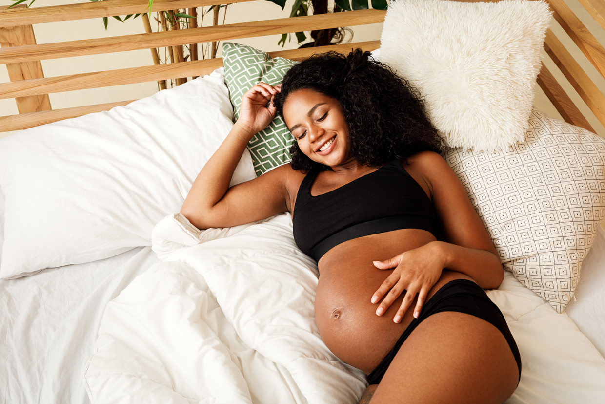 Smiling Pregnant Woman Lying On Bed At Home
