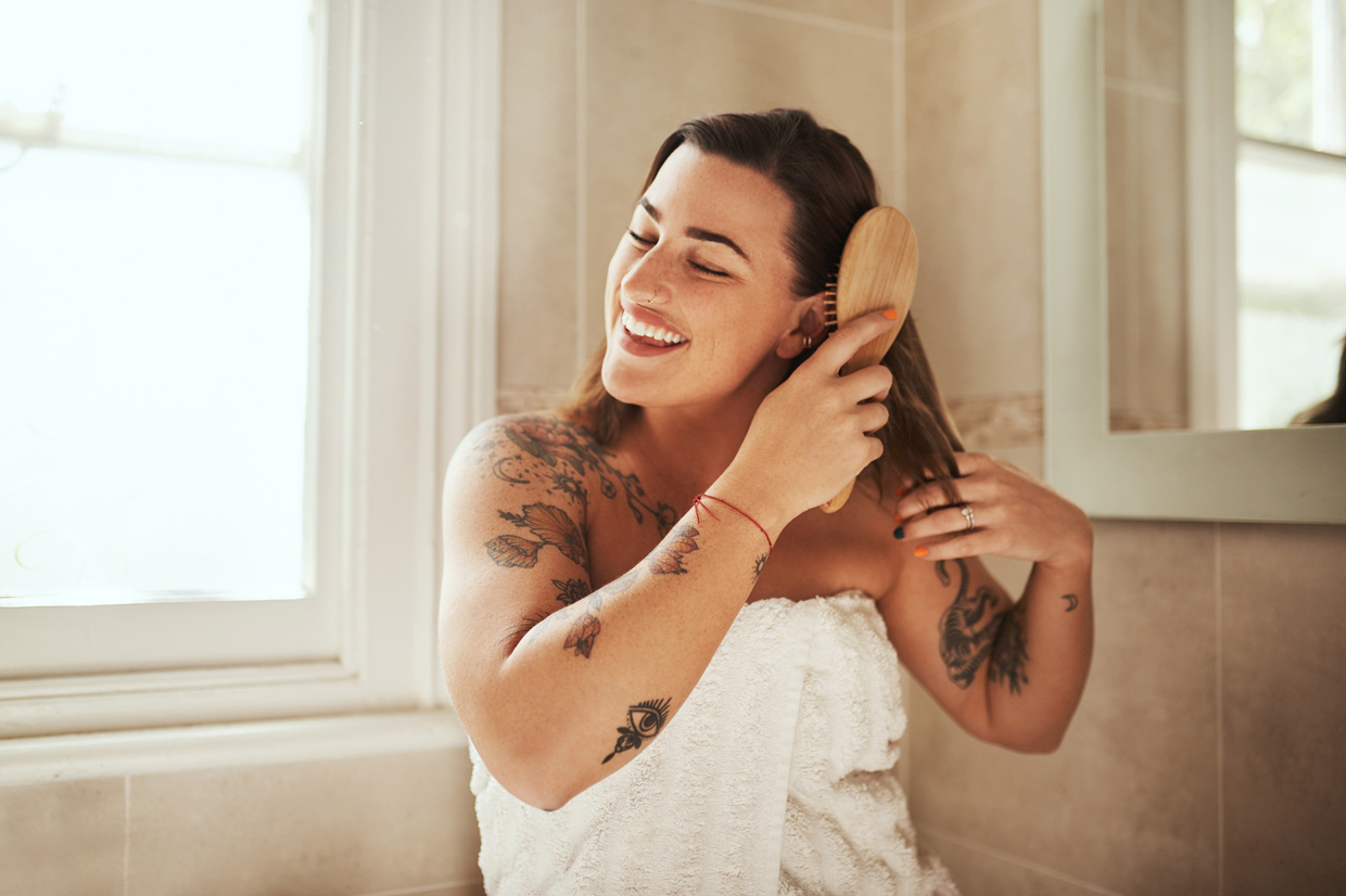 young woman with tattoos brushing hair inside bathroom