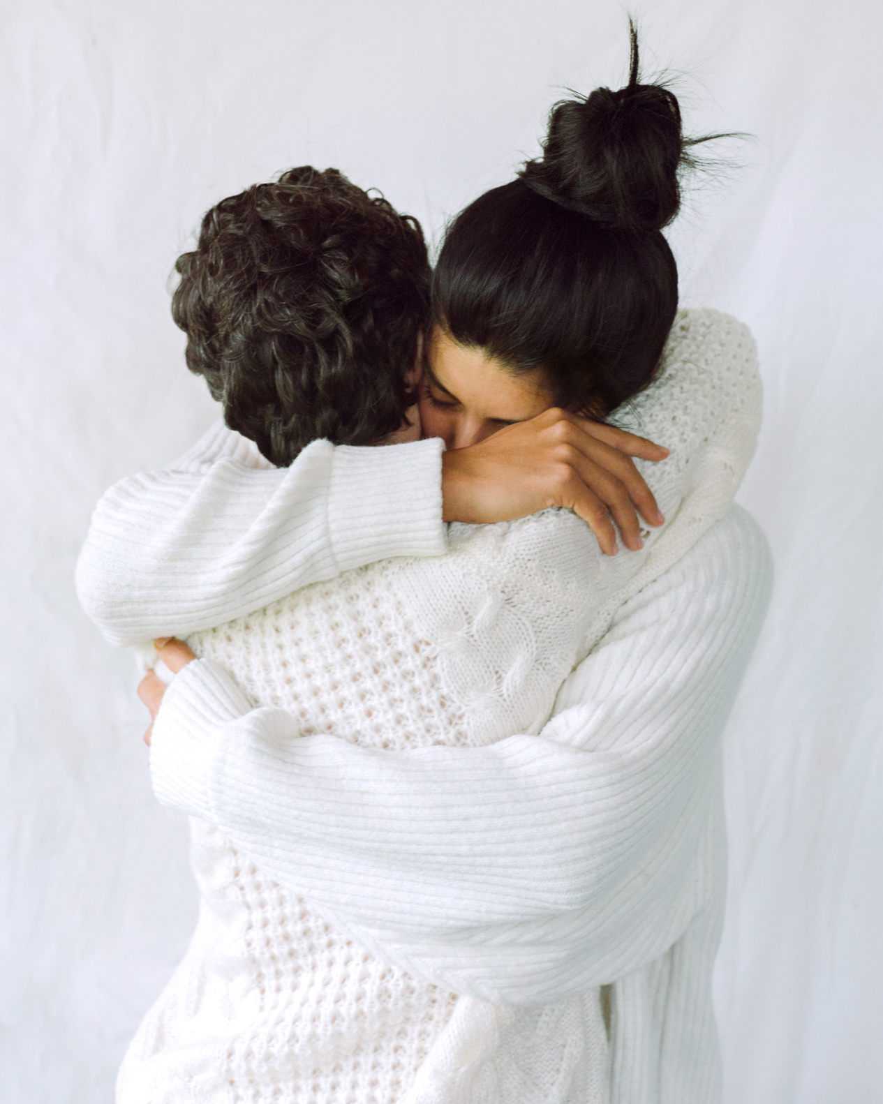 two women in white sweaters hugging
