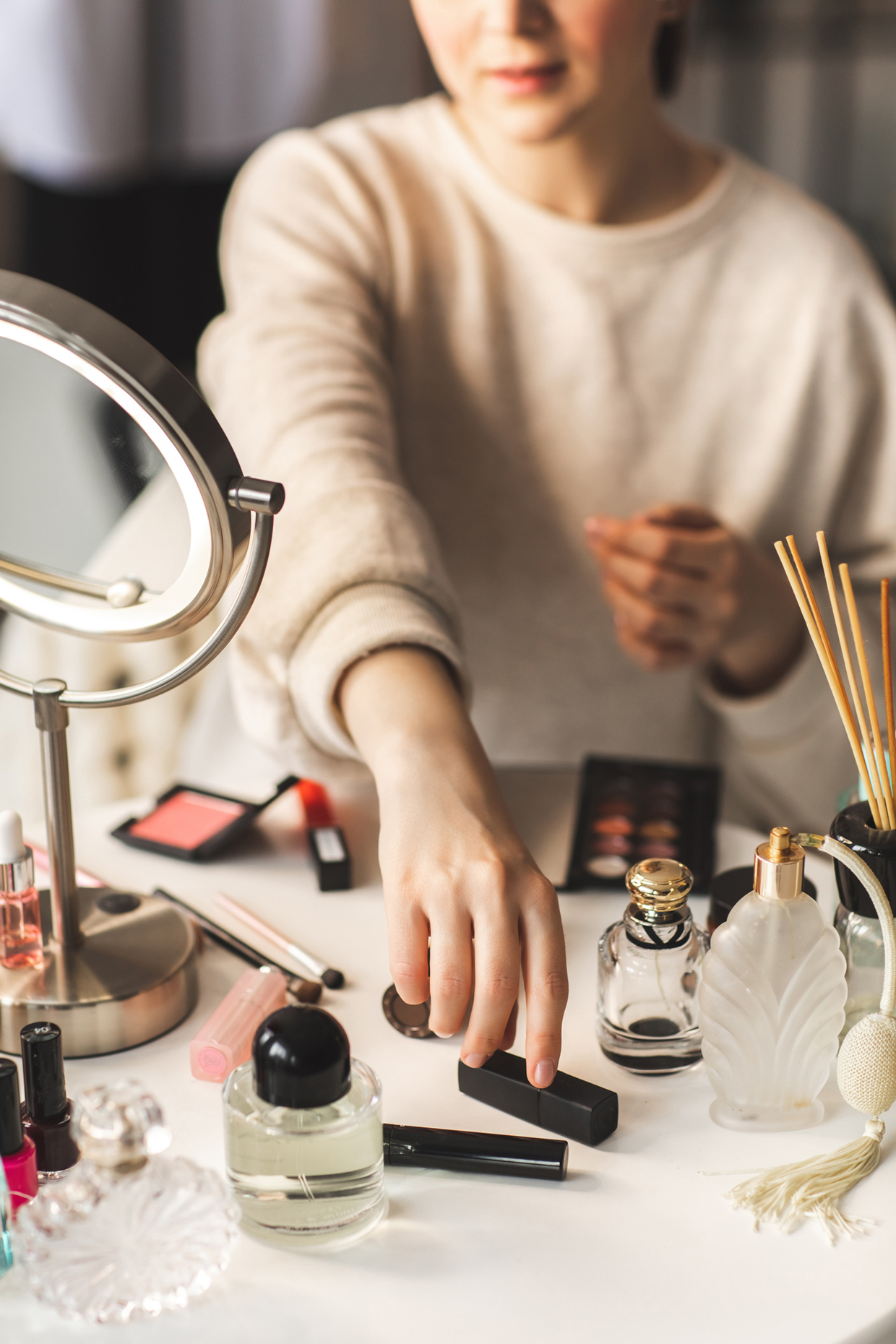 woman's hand is reaching out to pick up a lipstick from a table full of beauty products