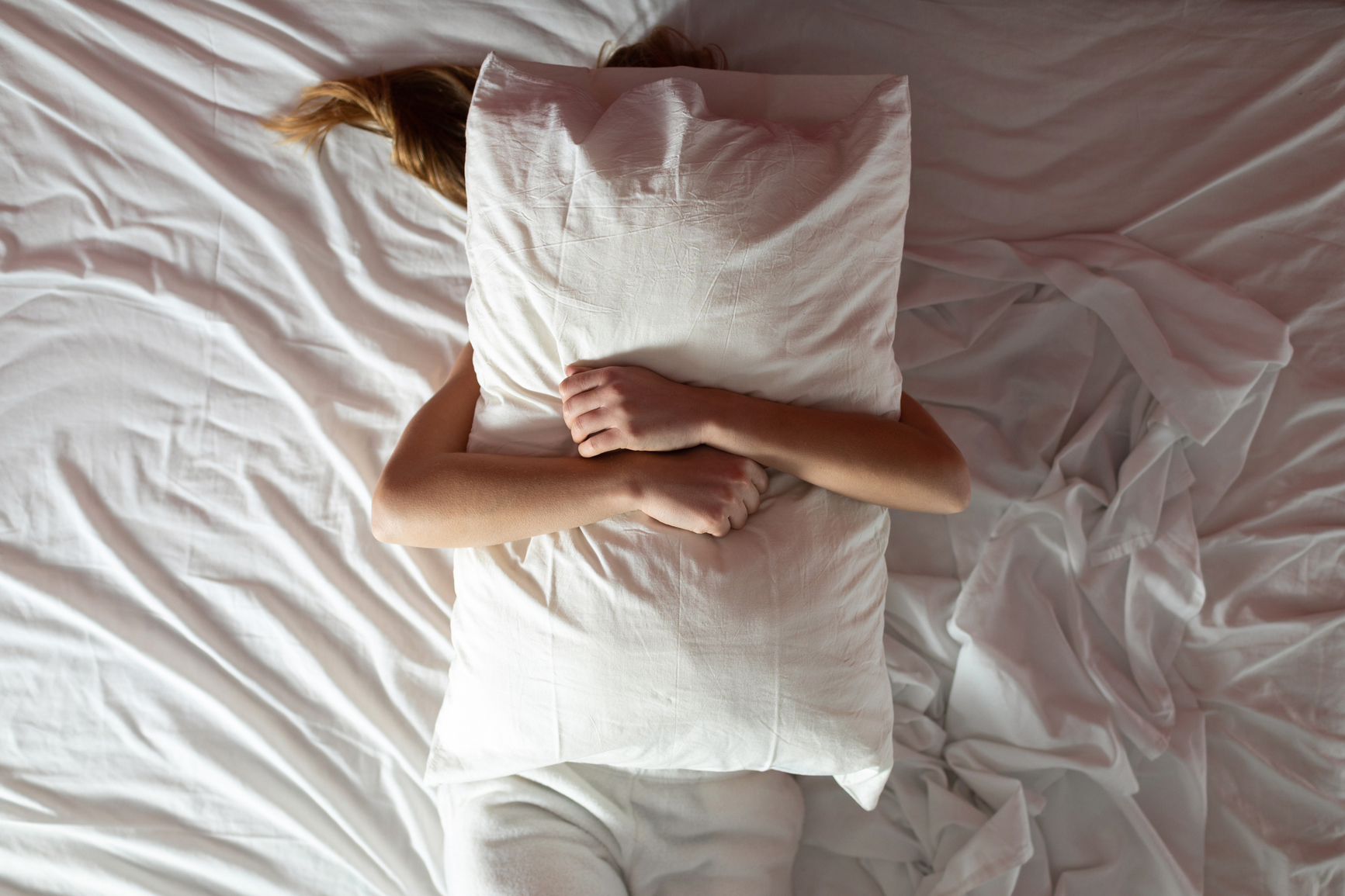 Woman covered with pillow her face and body in a white bed