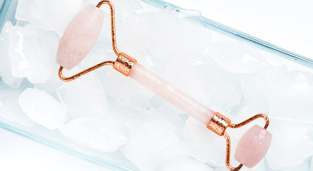 Cold rose quartz roller for facial massage lies in ice cubes
