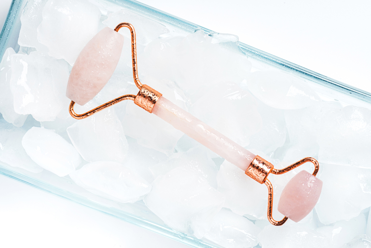 Cold rose quartz roller for facial massage lies in ice cubes