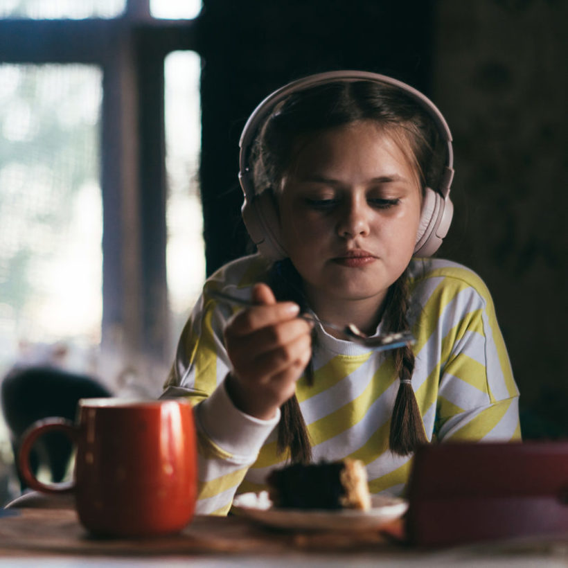 girl with headphones eating and watching tablet