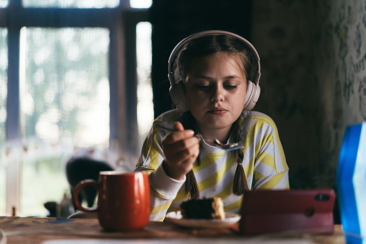 girl with headphones eating and watching tablet