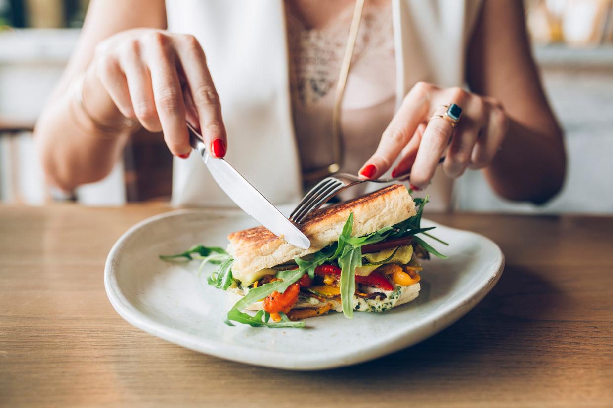 woman eating a veggie sandwith with fork and knife
