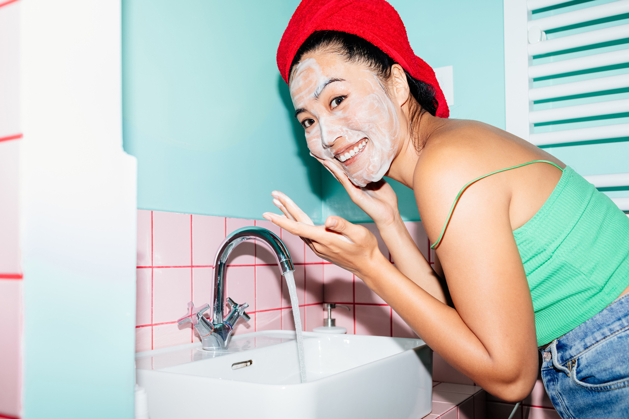 woman smiling while washing face in blue bathroom