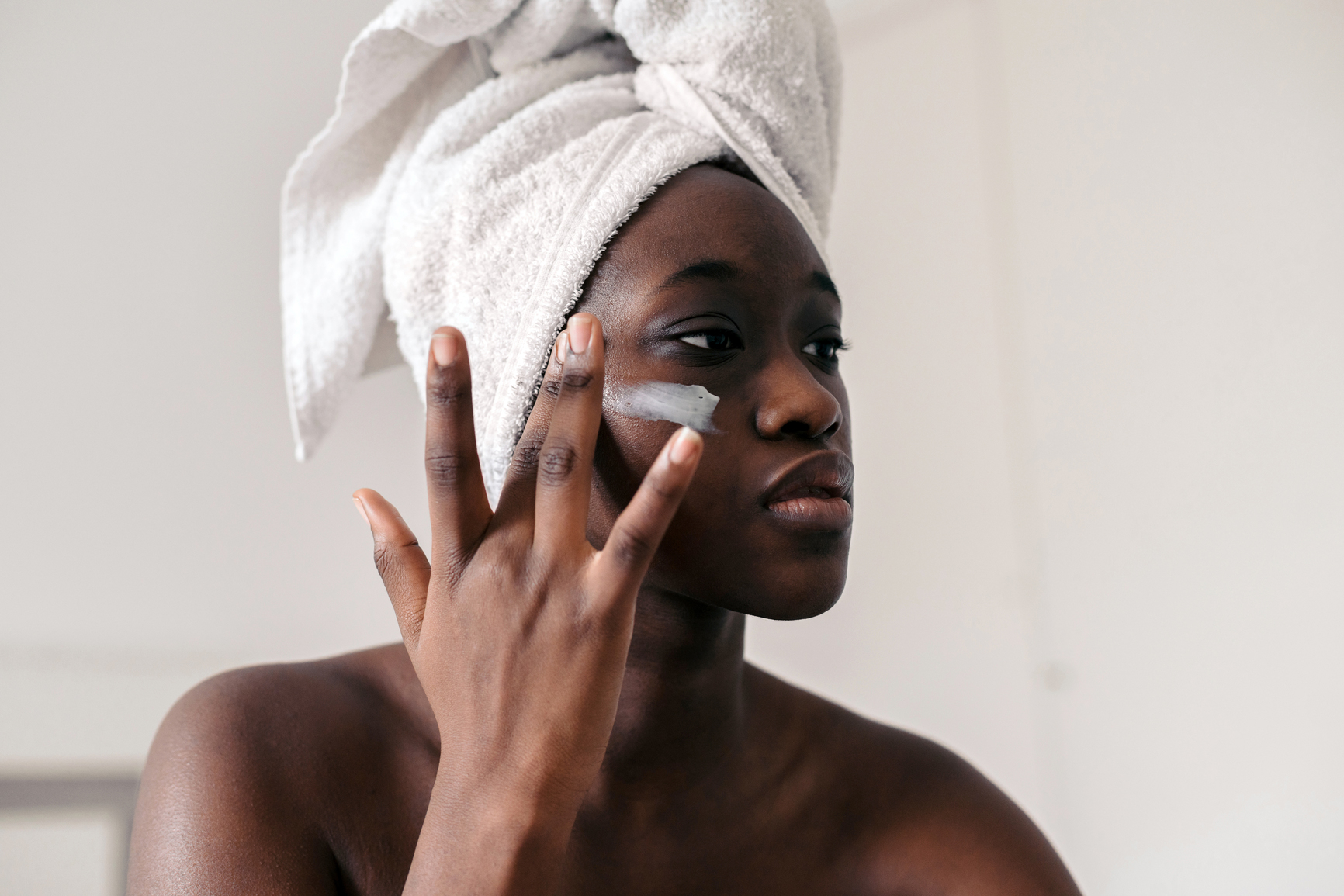 woman applying moisturizer in bedroom