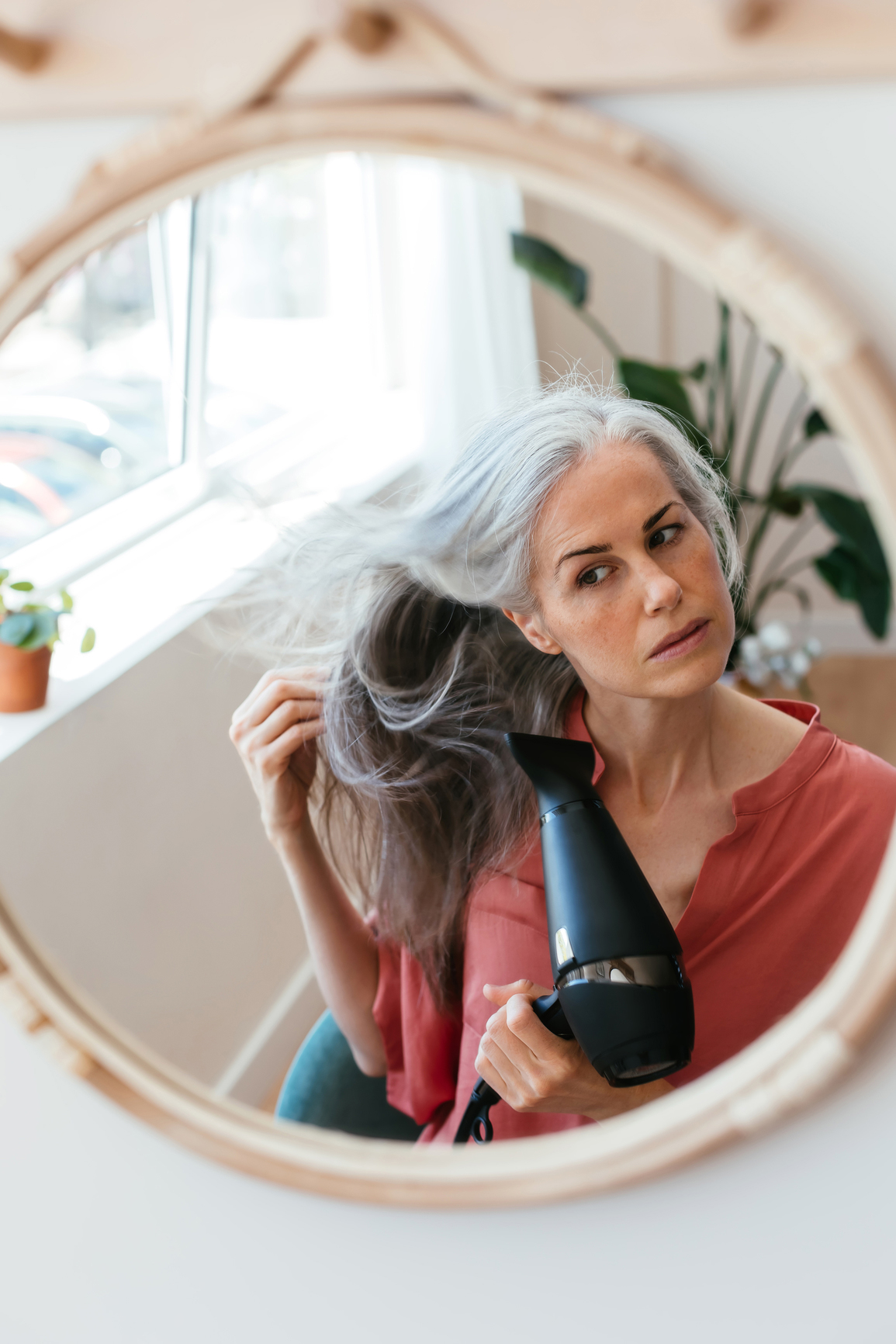 woman blow drying her hair in front of mirror