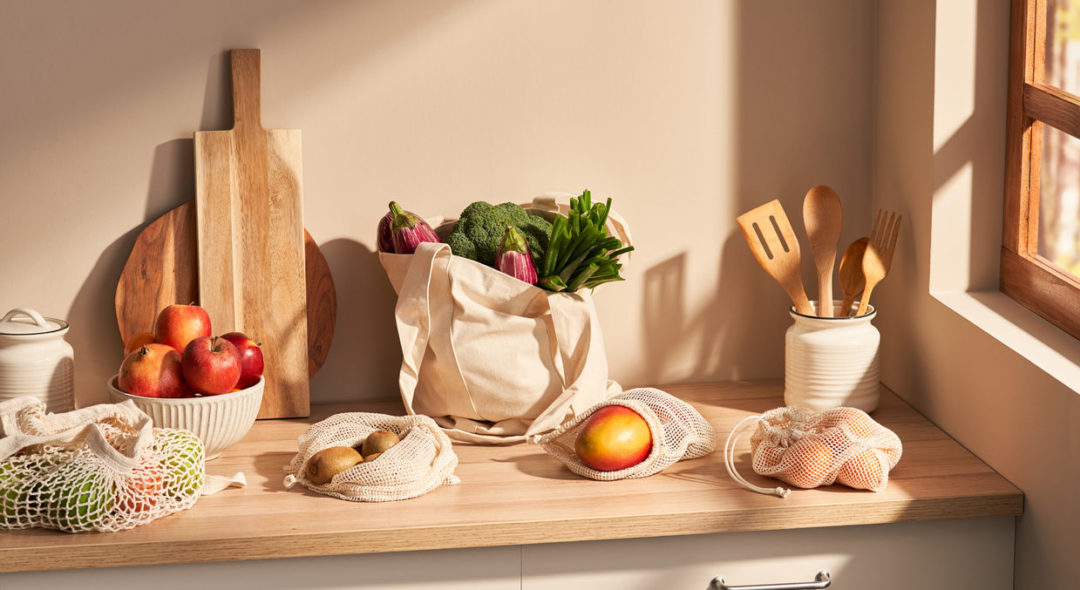Fresh fruits and vegetables in reusable bags on kitchen