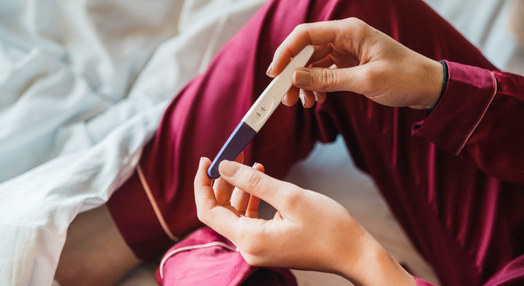 woman in bed looking at pregnancy test